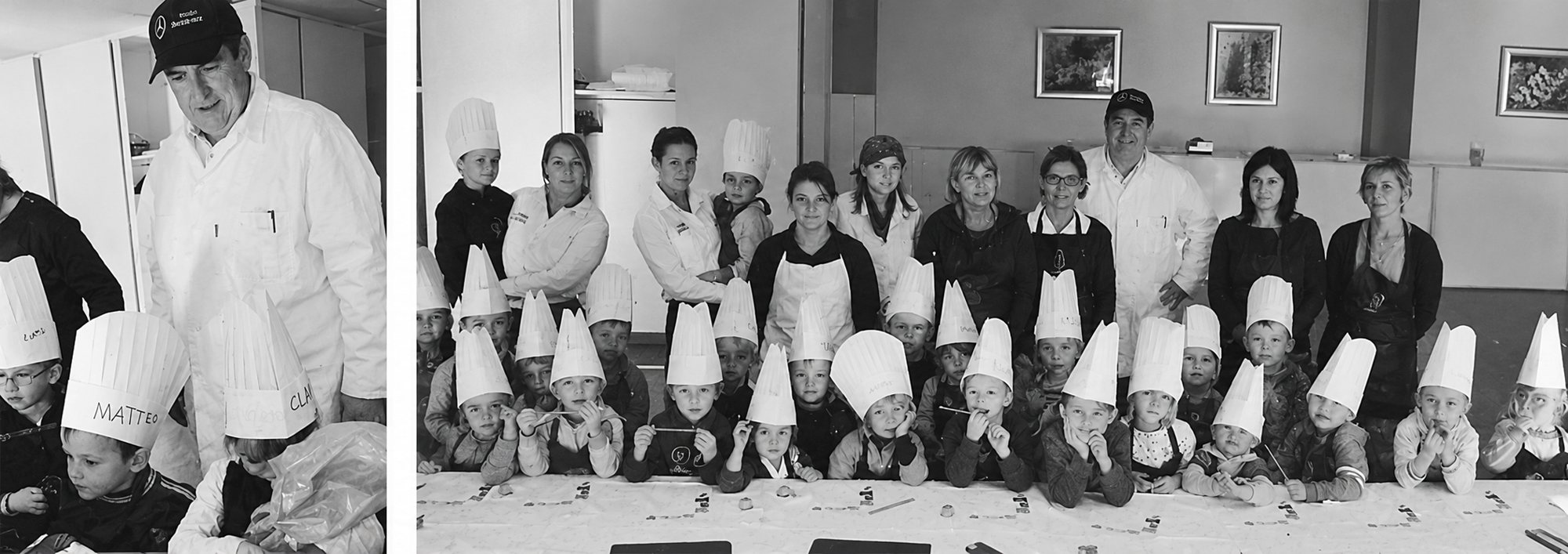 Photographie en noir et blanc d’un atelier de cuisine où de jeunes enfants portent des toques en papier, entourés d’adultes en blouse et en tablier.